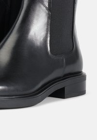 Zwarte leren Chelsea-boot met elastische zijkanten, ronde neus en een lage blokhak. Glad oppervlak met minimale stikseldetails.