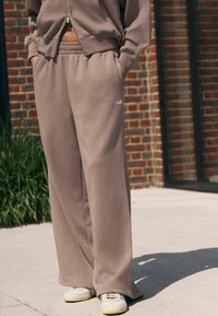 Brune brede sweatpants lavet af blødt stof, med elastisk talje og sidelommer. Parret med lyse sneakers.