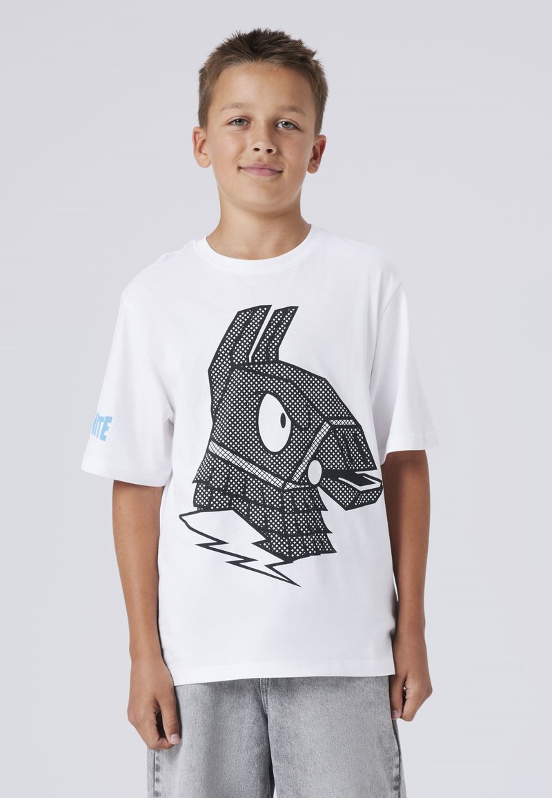 Boy wearing white t-shirt with large black graphic of a stylized llama head and lightning bolt, paired with light gray shorts.