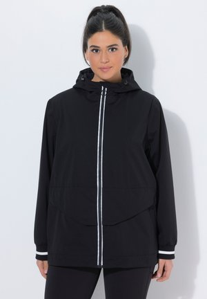 Giacca nera con cappuccio e zip frontale, caratterizzata da dettagli a strisce bianche e una vestibilità comoda. Il materiale sembra leggero, adatto per essere indossato a strati.