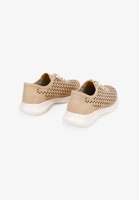 Zapatillas perforadas beige con cortes en forma de triángulo, forro interior en contraste y suela de goma blanca, con diseño de cordones y textura suave.