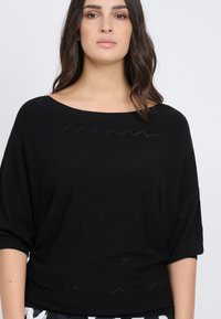 Maglietta nera a maglia con scollo ampio e maniche corte, caratterizzata da motivi a zigzag intagliati lungo il corpo per aggiungere texture.