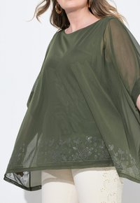 Top trasparente verde oliva con ricami floreali in argento lungo l'orlo. Presenta un collo rotondo e maniche ampie e fluide.