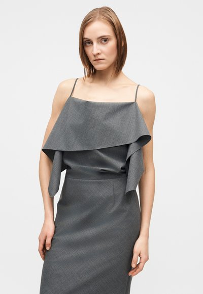 Robe grise avec un haut superposé à volants, des bretelles spaghetti et une jupe ajustée. Le tissu présente une texture subtile et un motif délicat.