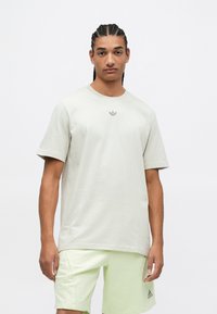 Svetlošedé bavlnené tričko s krátkymi rukávmi a okrúhlym výstrihom, s malým čiernym logom Adidas na hrudi.
