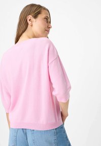 Maglioncino rosa chiaro a maniche corte in materiale morbido con vestibilità ampia e scollatura larga, abbinato a shorts in denim a vita alta.