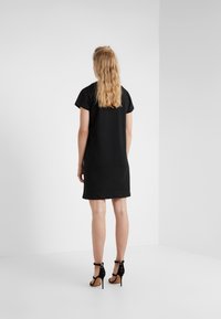 Musta lyhythihainen mekko, jossa on suora leikkaus ja sileä pinta. Yhdistettynä korkeakorkoisiin mustiin sandaaleihin, joissa on nilkkakahvat ja pyöreät korostukset.