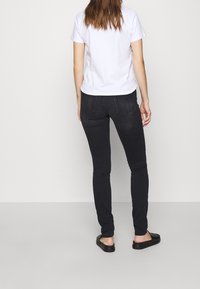 Jeans pitillo negros con un diseño clásico, con textura suave, dos bolsillos traseros, combinados con una camiseta blanca y sandalias negras.