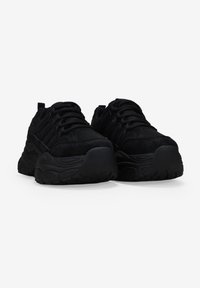 Las zapatillas negras cuentan con una parte superior texturizada hecha de materiales de malla y ante, una suela moldeada con detalles pronunciados y un diseño con cordones.