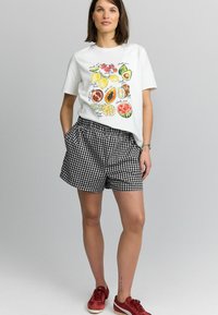 T-shirt en coton blanc avec des illustrations de fruits colorés ; associé à un short en vichy noir et blanc ; des baskets rouges complètent la tenue.