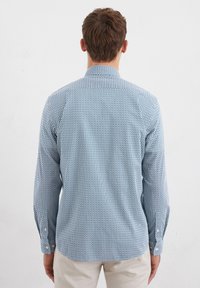Long-sleeve shirt featuring a blue and white geometric pattern, buttoned cuffs, and a classic collar. Fabric appears lightweight and smooth.