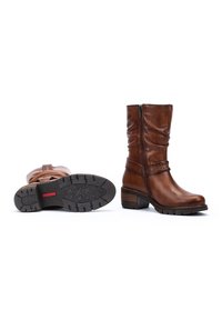 Bottines en cuir marron avec une fermeture éclair sur le côté, texture plissée, une sangle décorative, et une semelle en caoutchouc texturé avec un motif d'étoiles.