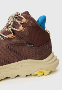 Brun vandringsko med en texturerad ovandel, Gore-Tex-märke, kontrasterande blå tunga och gul Vibram-sula för grepp.