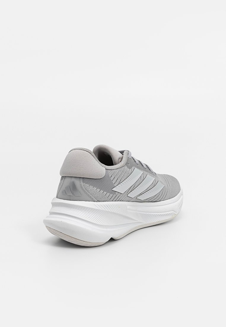 Hellgrau sportlicher Sneaker mit weißer Sohle und drei weißen Streifen an der Seite, von der hinteren linken Ecke auf einem weißen Hintergrund betrachtet.