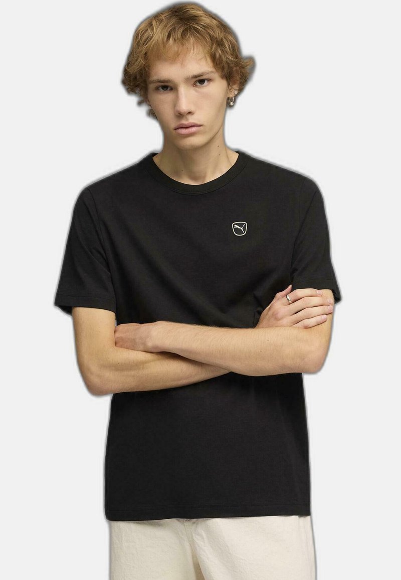 T-shirt en coton noir avec un petit logo brodé en forme de badge arrondi sur la poitrine. Manches courtes et col rond.