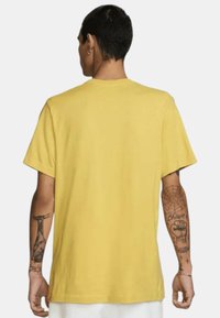 Camiseta de algodón amarilla con un corte relajado, mangas cortas y un dobladillo recto. Presenta tatuajes visibles en los brazos.