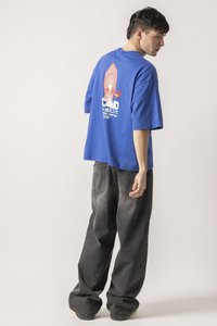 Blue oversized t-shirt with red graphic design on back; paired with black baggy jeans and casual beige sneakers.