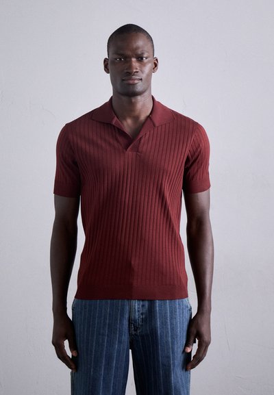 Polo shirt bordeaux à manches courtes côtelé avec un col en V et un col plat. Associé à un jean bleu à rayures. Texture lisse, design ajusté.