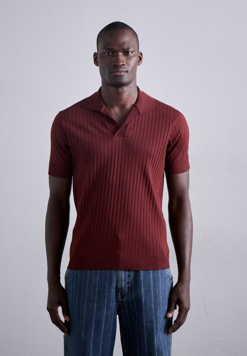 Polo shirt bordeaux à manches courtes côtelé avec un col en V et un col plat. Associé à un jean bleu à rayures. Texture lisse, design ajusté.