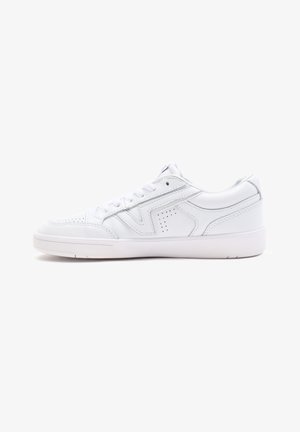 Niski, biały skórzany sneaker z zapięciem na sznurówki, perforowanymi detalami i płaską gumową podeszwą, pokazany z profilu na białym tle.