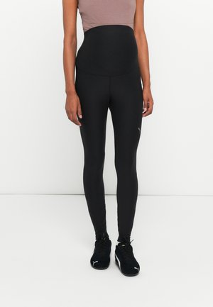 Svarta högmidjade leggings i stretchmaterial, med en sömlös design och åtsittande silhuett, kombinerade med svarta träningsskor.