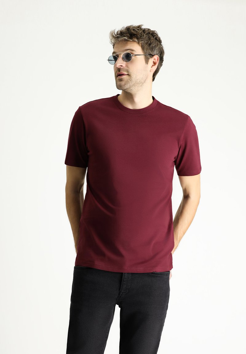 Camiseta de manga corta burdeos hecha de una tela suave con cuello redondo; combinada con unos jeans negros informales y unas gafas de sol redondas oscuras.