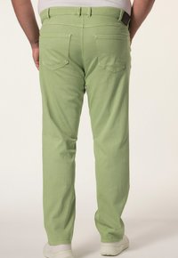 Pantalones verde claro de pierna recta con una textura suave, que cuentan con bolsillos traseros y una cinturilla con pasadores para el cinturón. Llevados con zapatos blancos.