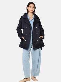 Navy double-breasted trench coat with large gold buttons, front pockets, and a hood, worn over a light blue denim outfit.