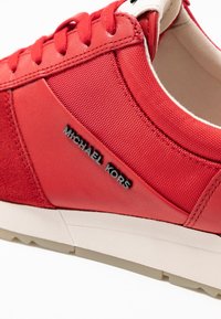 Baskets rouges en cuir et textile, avec un corps texturé, des lacets plats, une semelle blanche et un logo "Michael Kors" embossé.