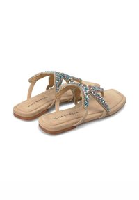 Sandalias planas beige con tiras adornadas con cristales, con punta cuadrada y textura similar a la gamuza. Nombre de la marca "ALMA EN PEÑA" en la plantilla.
