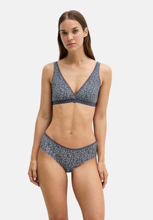 Woman wearing matching blue floral bralette and high-cut briefs standing against plain background.