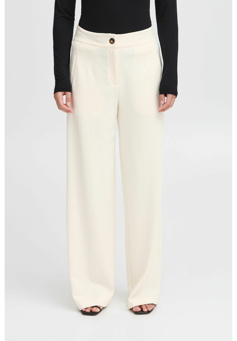 Witte, gestructureerde wijduitlopende broek met een hoge taille, voorzien van voorzakken en een enkele knoopsluiting. Gecombineerd met een zwart langslijf top.
