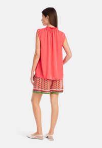 Coral sleeveless top with gathered neckline, paired with patterned shorts featuring red strawberry design and green accents; white footwear.
