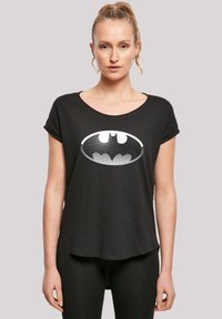 Svart t-skjorte med kort erme og vid hals, med et hvitt Batman-logo i halftone-mønster på forsiden, laget av myk stoff.