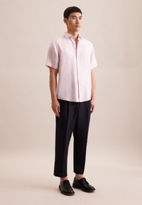 Lichtroze, kortärmige linnen shirt met knoopsluiting aan de voorkant, gecombineerd met donkerblauwe, losse broek en zwarte leren schoenen.