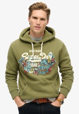 Sweat-shirt à capuche vert olive en tissu doux, avec un imprimé graphique représentant des motifs floraux et un masque bleu, capuche avec cordon et poche avant.