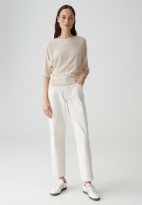 Helles beigefarbenes Strickoberteil mit lockerer Passform und Rundhalsausschnitt, kombiniert mit weißen, geraden Hosen und weißen Sneakers. Einfaches Design, keine Muster.