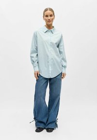 Chemise boutonnée à rayures bleu clair avec manches longues et col, associée à un jean en denim à jambes larges avec des détails noués à l'ourlet.