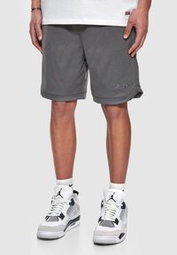 Shorts en maille grise avec un ourlet plié et un détail de logo subtil, associés à des baskets athlétiques blanches et noires présentant un design en mesh.