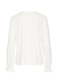 Blouse blanche à manches longues en tissu ajouré, col rond et poignets volantés sur fond uni, vue de dos.