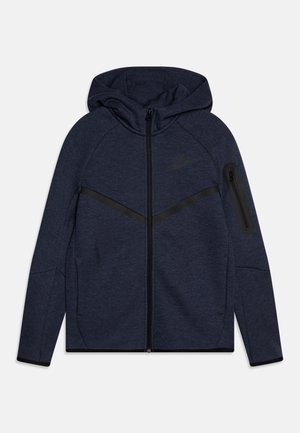 Felpa con zip di colore blu scuro realizzata in tessuto texturizzato. Presenta un cappuccio, accenti neri diagonali e una tasca con zip sul manica sinistra.