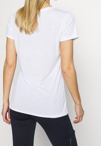 Vit kortärmad t-shirt med rund hals, mjuk textur och avslappnad passform, med fokus på rygg- och axeldetaljer.