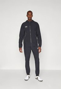 Chándal deportivo azul marino hecho de tela ligera, que incluye una chaqueta con cremallera con detalles blancos y logo, combinado con pantalones a juego.