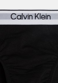 Čierne bavlnené spodné prádlo s širokým bielym pásom s textom "Calvin Klein" v čiernej farbe. Hladká textura s elastickým rozťahovaním.