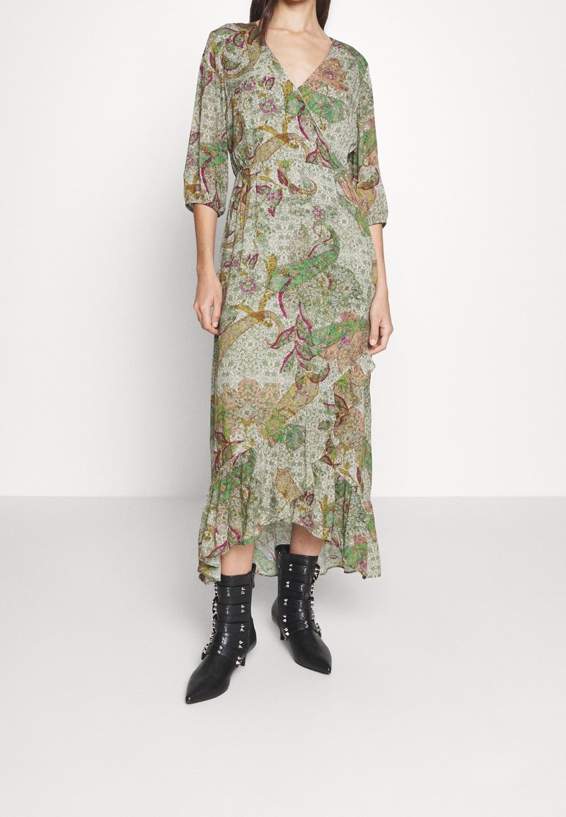 Femme portant une longue robe portefeuille fleurie avec des manches 3/4 et un ourlet à volants, associée à des bottines noires à bout pointu avec des détails de boucle.