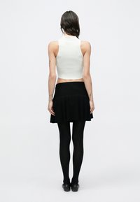 Biele rebrované tielko bez rukávov v krátkej dĺžke, skombinované s čiernou rozšírenou sukňou, nosené s čiernymi pančuchami a čiernymi balerínami. Jednoduchý dizajn bez vzorov.