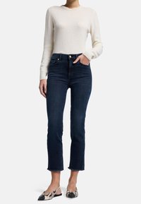 Jean en denim foncé à taille haute, longueur cropped et ourlet effiloché ; assortis à un pull léger blanc et des baskets à enfiler imprimées.