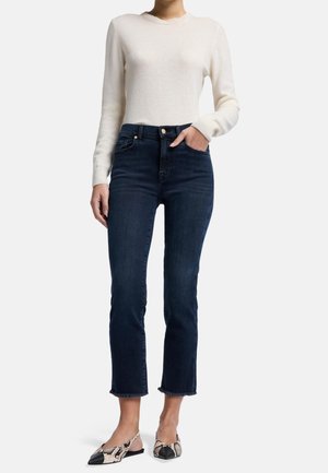 Jean en denim foncé à taille haute, longueur cropped et ourlet effiloché ; assortis à un pull léger blanc et des baskets à enfiler imprimées.