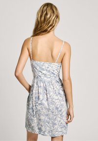 Floral dress in white and blue, with thin straps, gathered waist, and a short flowy skirt, featuring a botanical print throughout.