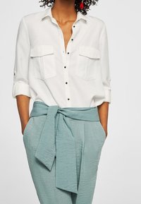 Hvid skjorte med opolstrede ærmer og to brystlommer, parret med lys blå teksturerede bukser med en bundet taljedetalje.